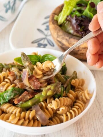 A fork with creamy vegetable pasta being lifted out of a bowl of the pasta.