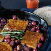 Cast iron skillet with tempeh, caramelized onions, and grapes in it. Garnished with fresh rosemary.