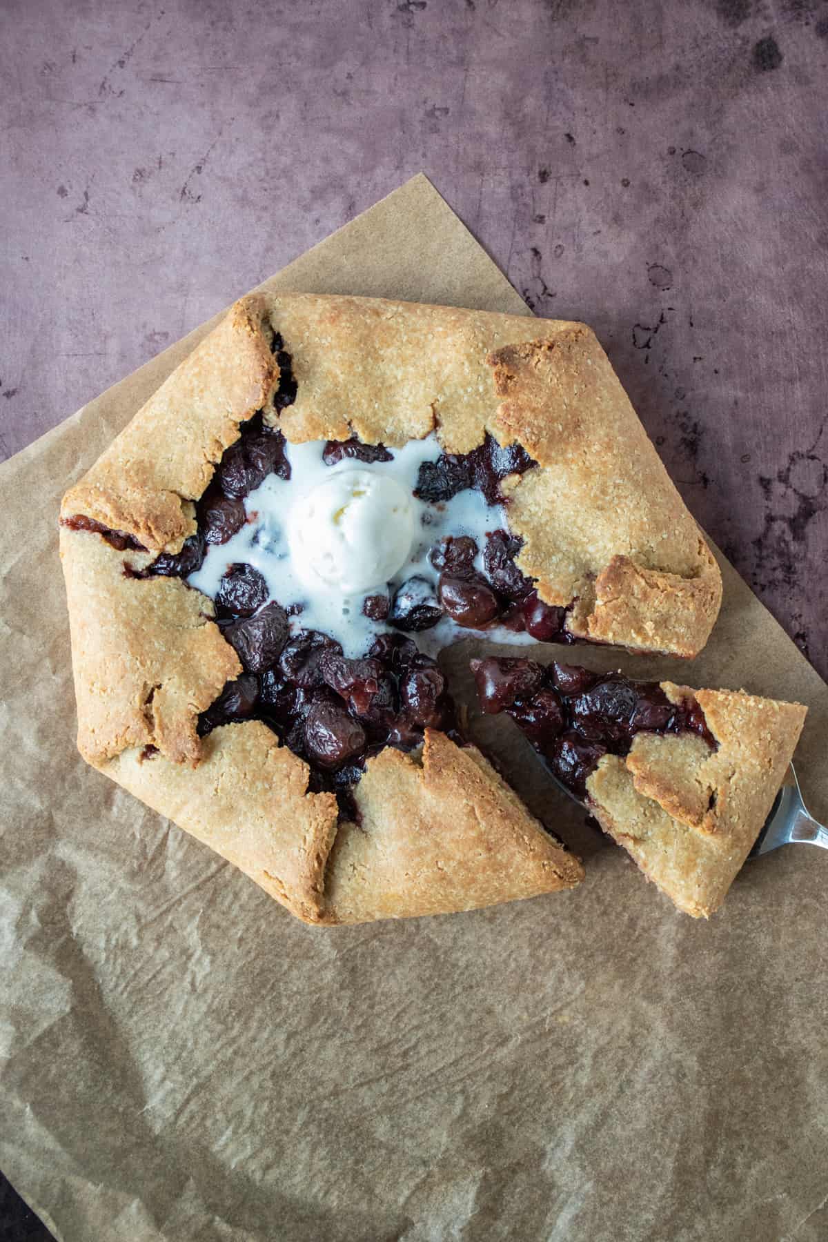 Overhead shot of cherry galette with melted ice cream on top, and a serving utensil removing a slice.