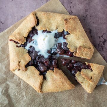 Overhead shot of cherry galette with melted ice cream on top, and a serving utensil removing a slice.