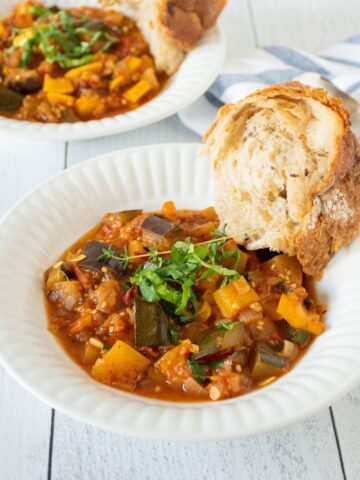 Two bowls of ratatouille with crusty bread on the side.