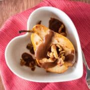 Half of a baked pear in a dish, drizzled with chocolate sauce and toasted walnuts.