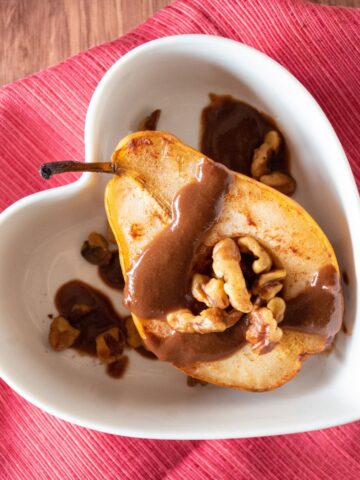 Half of a baked pear in a dish, drizzled with chocolate sauce and toasted walnuts.