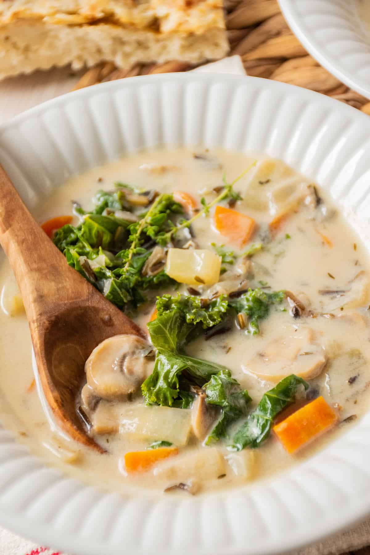 Bowl of creamy mushroom soup with kale, with a wooden spoon in the bowl.