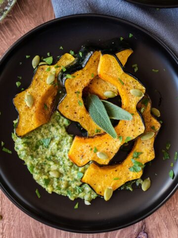 Slices of roasted acorn squash on a plate over sage pesto with pepitas.