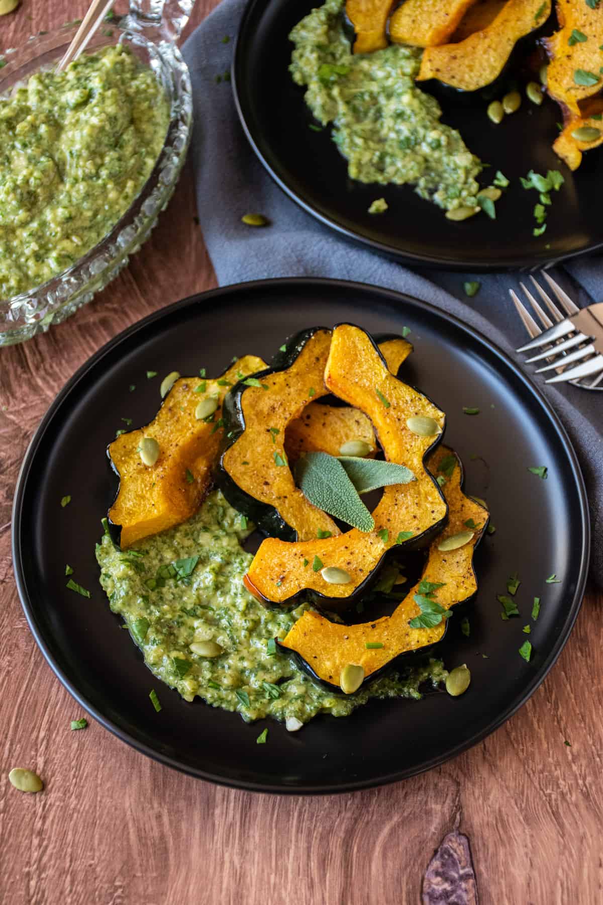 Slices of roasted acorn squash on a plate over sage pesto with pepitas.