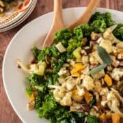 Large serving dish with kale and cauliflower on it, with serving utensils.