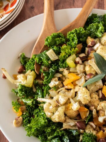 Large serving dish with kale and cauliflower on it, with serving utensils.