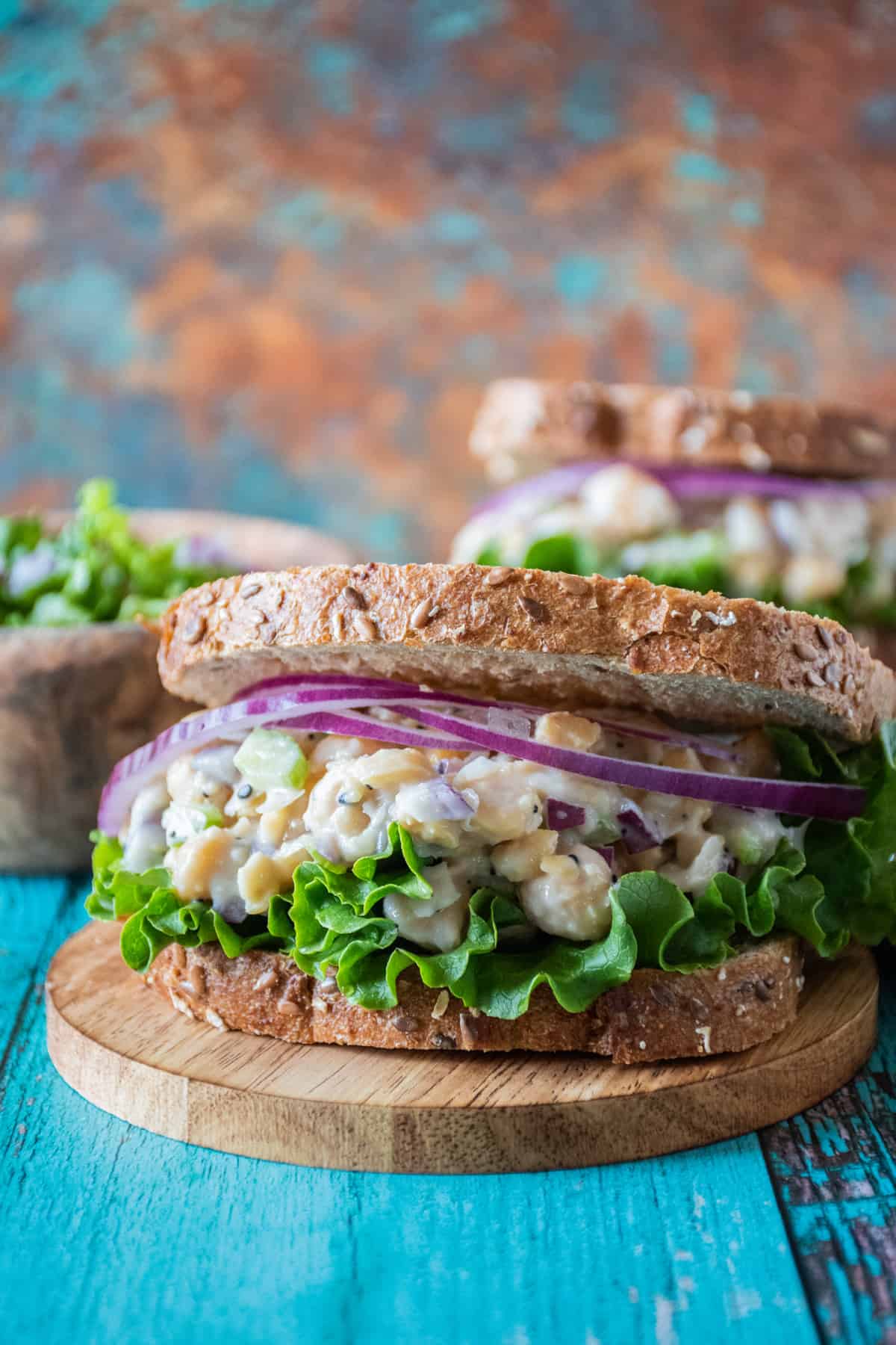 Sandwich with chickpea salad, lettuce, and red onion in it, sitting on a small round board.