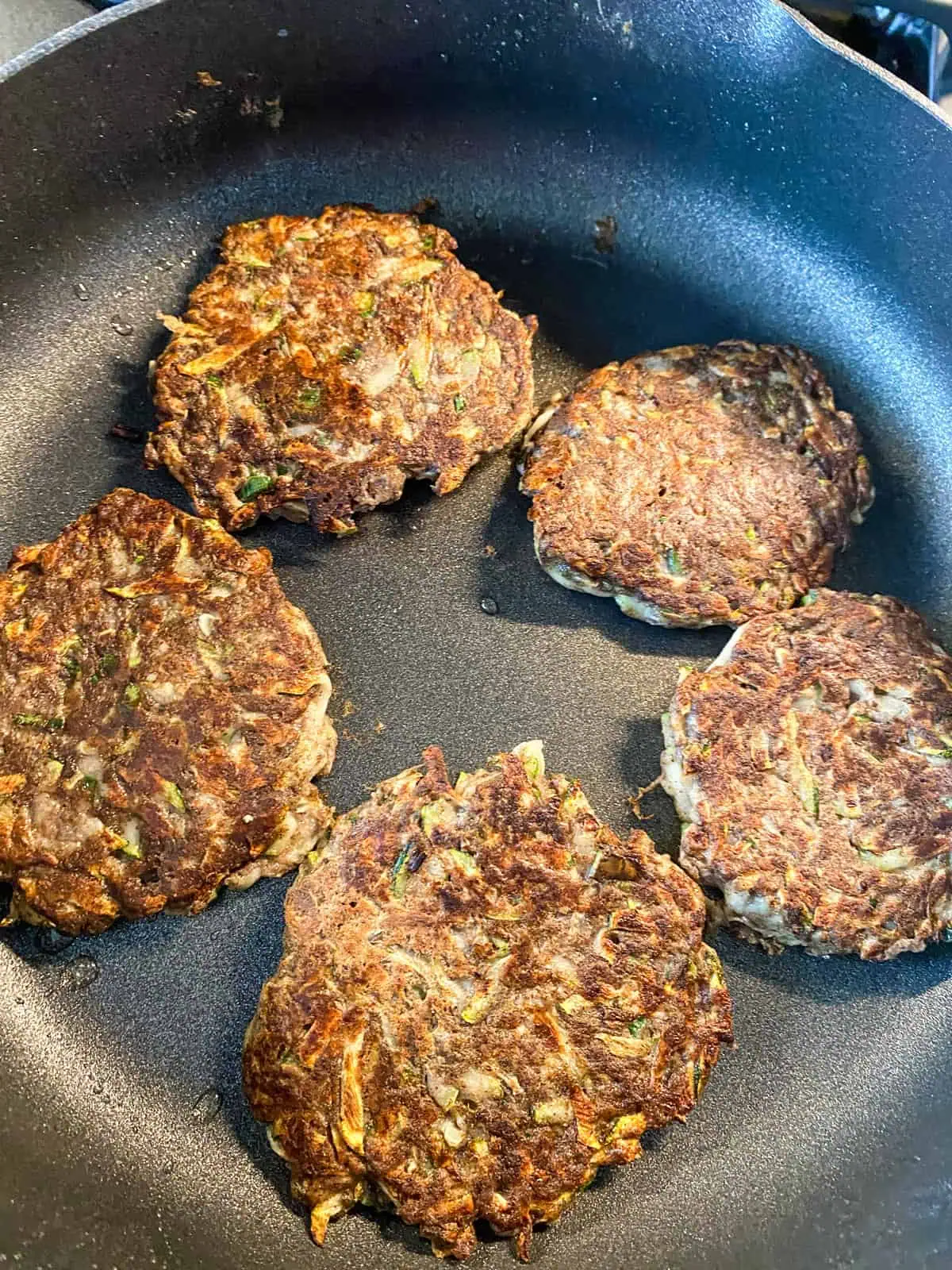 Fritters flipped to cook on the other side, in a large pan.
