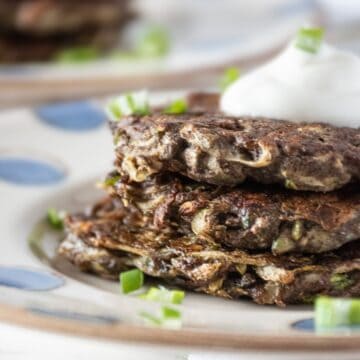 Close up of a stack of 3 zucchini fritters, topped with a dollop of plain Greek yogurt.