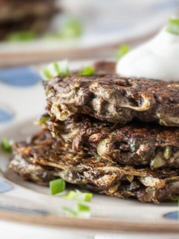 Close up of a stack of 3 zucchini fritters, topped with a dollop of plain Greek yogurt.