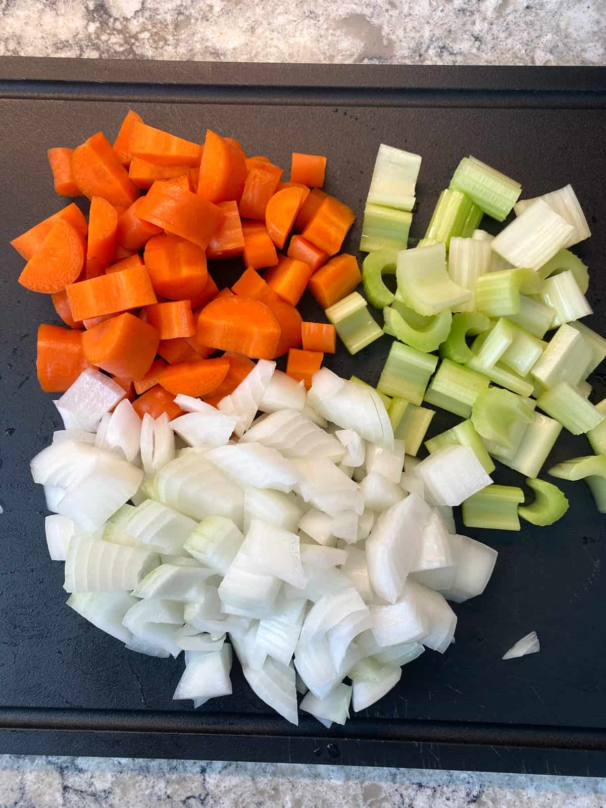 Chopped carrots, celery, and onion on a cutting board.