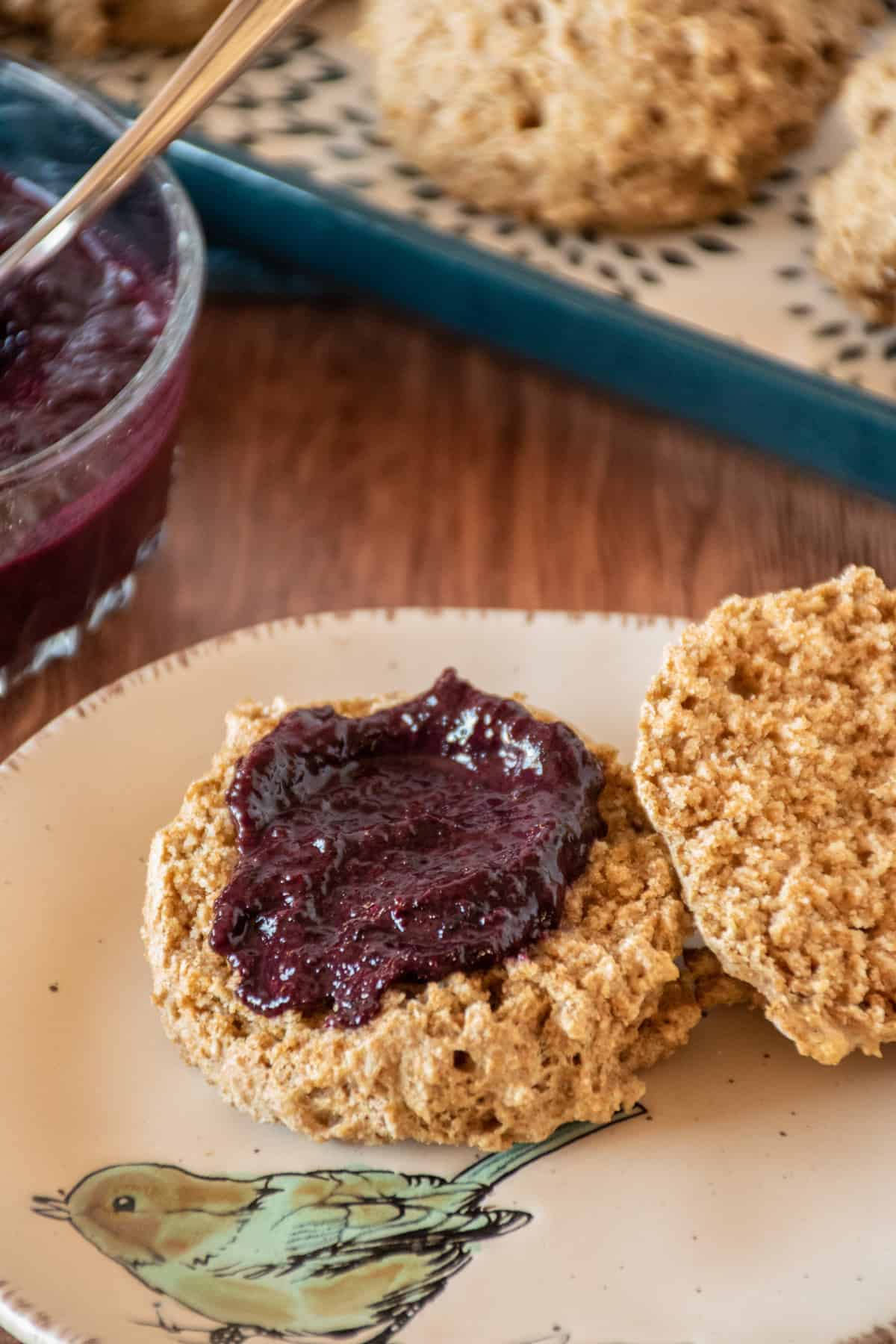 Biscuit, cut in half, with jam smeared on one half, on a small plate.