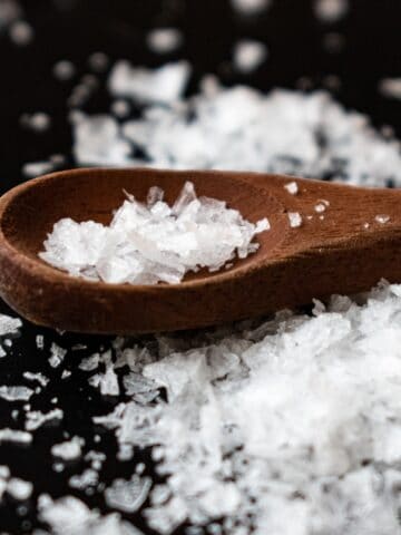 Small wooden spoon with salt in it, and around it.