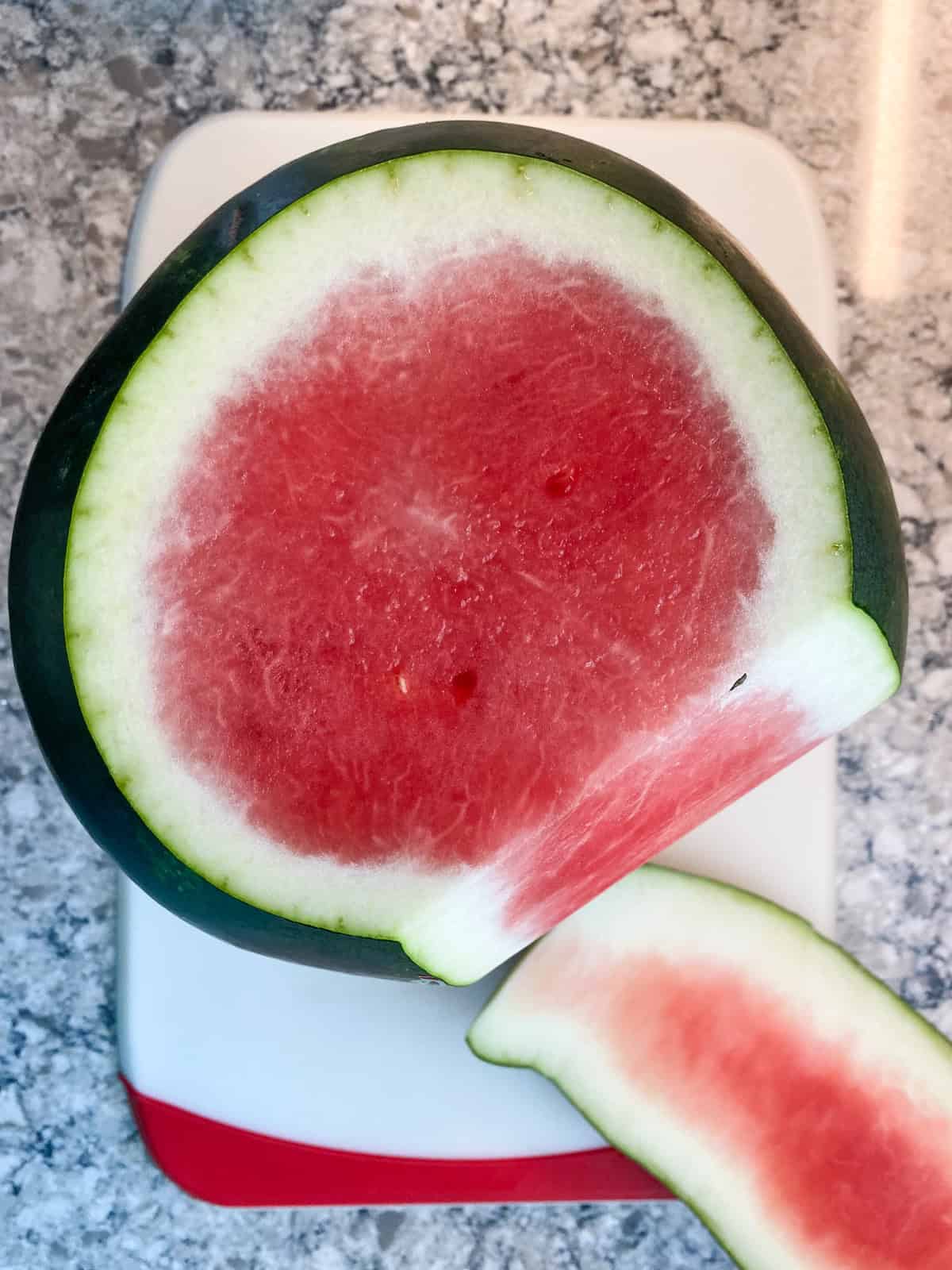 Whole watermelon, ends removed, stood upright with a slice of the green and white rind cut off from top to bottom.