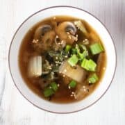 Overhead image of a bowl with bok choy and mushroom soup, garnished with sesame seeds.