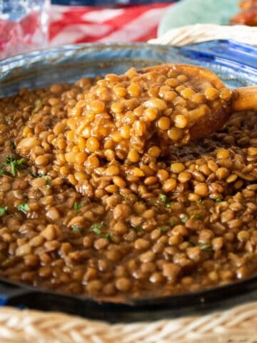 Glass baking dish with lentil baked beans and a wooden spoon scooping some.