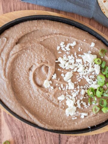 Refried beans in a small cast iron skillet, garnished with feta cheese and green onion slices.
