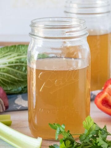 Vegetable stock in a mason jar, surrounded by fresh vegetables.