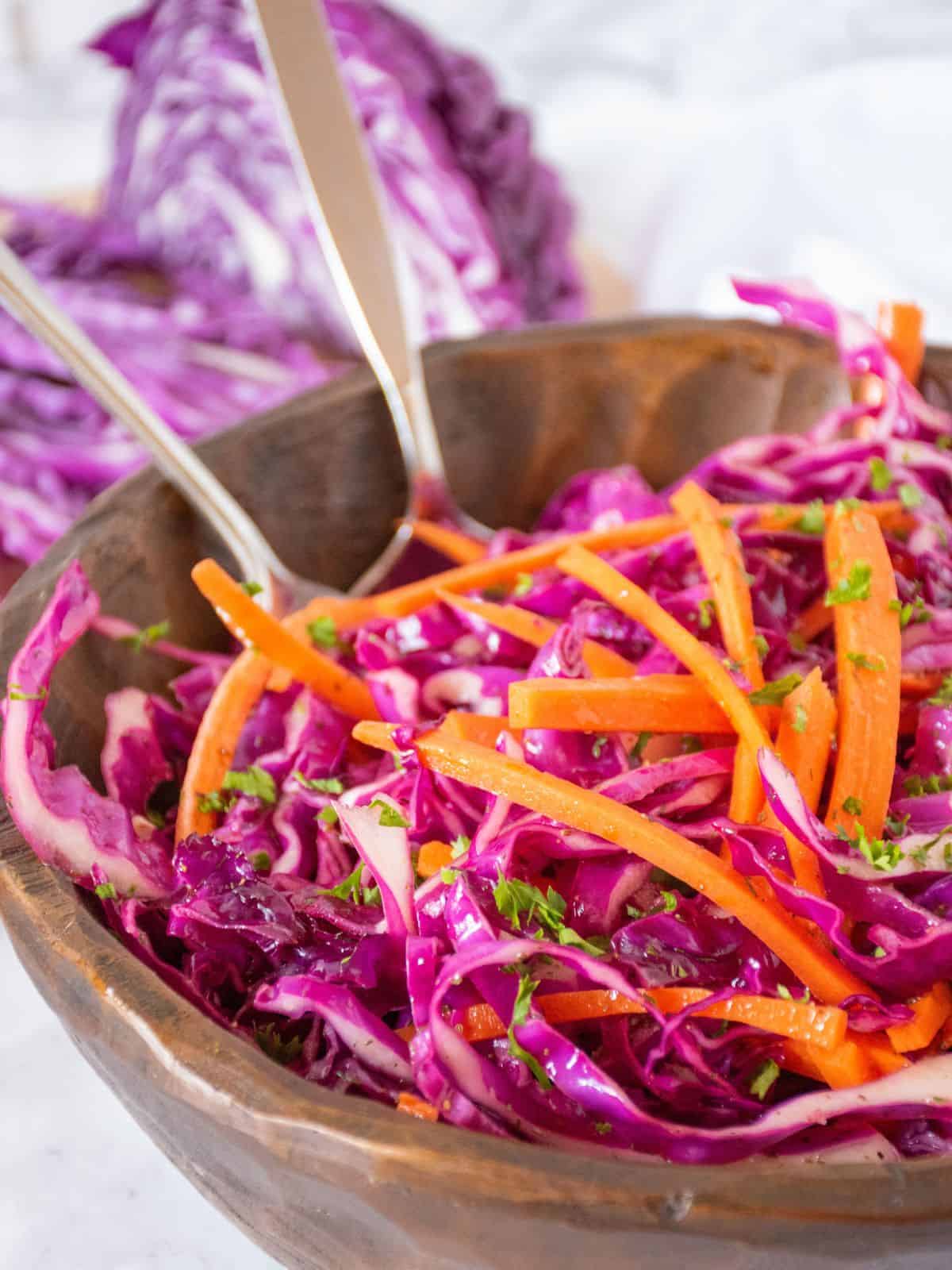 Wooden bowl with red cabbage coleslaw in it and two spoons for serving.