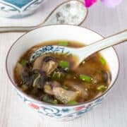 Bowl with bok choy and mushroom soup, garnished with sesame seeds.