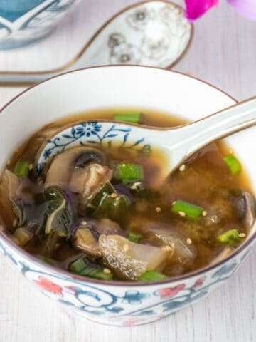 Bowl with bok choy and mushroom soup, garnished with sesame seeds.