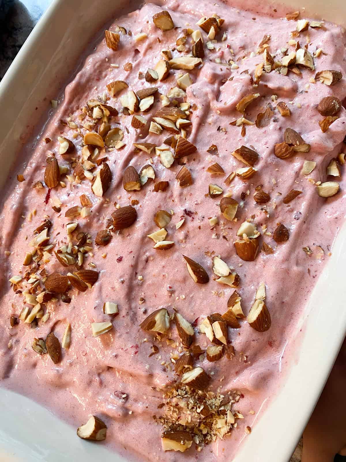 Processed cherry nice cream, topped with chopped almonds, in a freezer safe dish, ready for the freezer.
