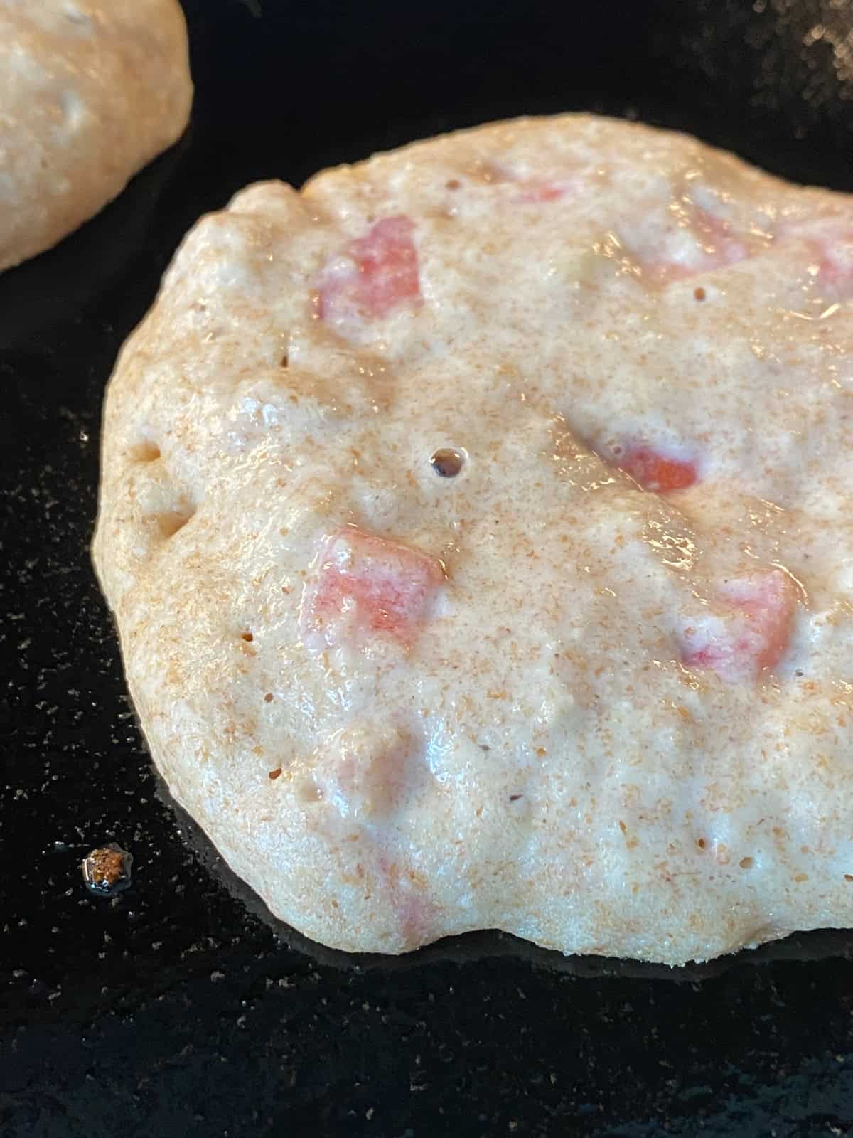 Pancake batter on a griddle, with bubbles visible, and the edges starting to dry out, revealing time to flip.