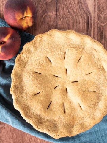 Overhead shot of a whole pie, with fresh peaches beside it.