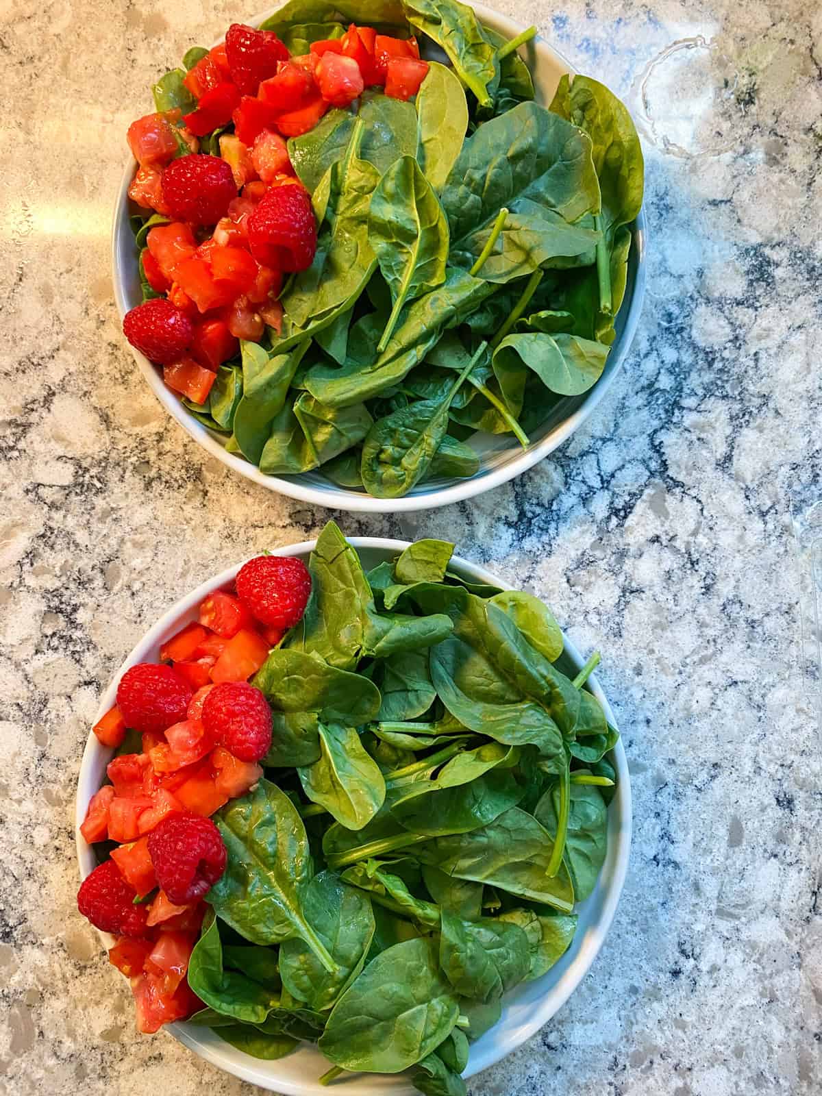 Two plates of salad with red raspberries and chopped tomatoes added in a column along the left side of the plate.