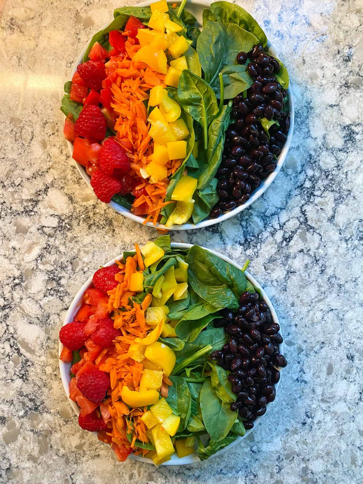 Two plates of salad with a column of yellow peppers and a column of black beans added.