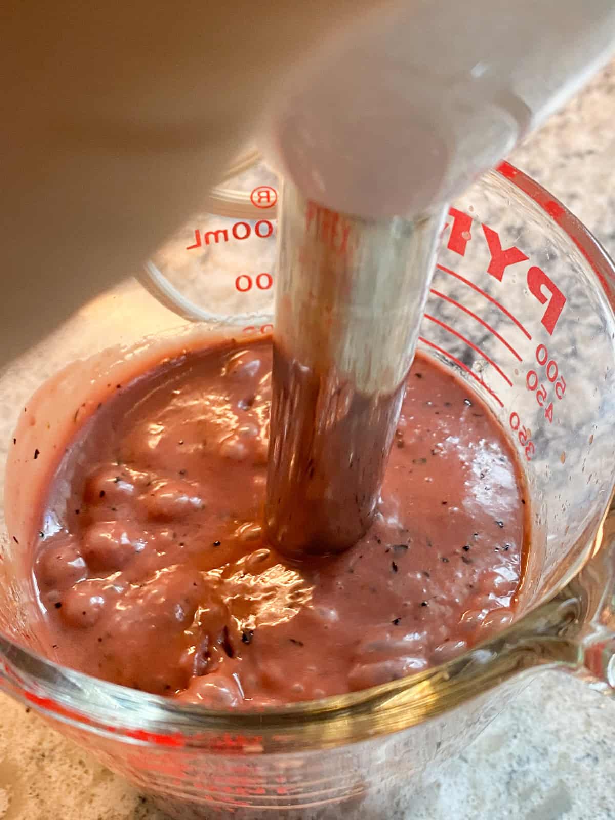 Blueberry dressing being blended with an immersion blender.