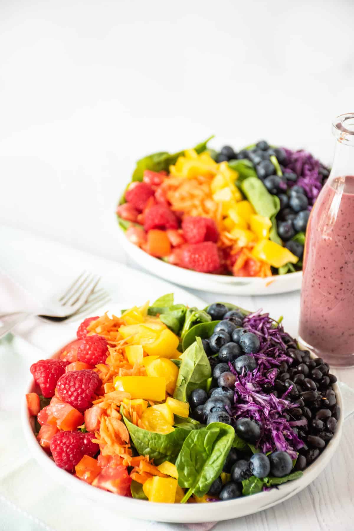 Salad with rainbow colored vegetables, and a bottle of blueberry dressing beside it.