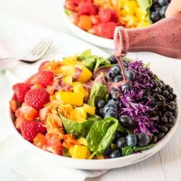 Salad with rainbow colored vegetables, and dressing being poured on.