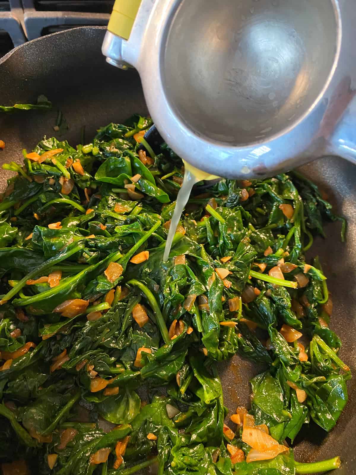Lemon juice being poured into the pan of sauteed spinach.