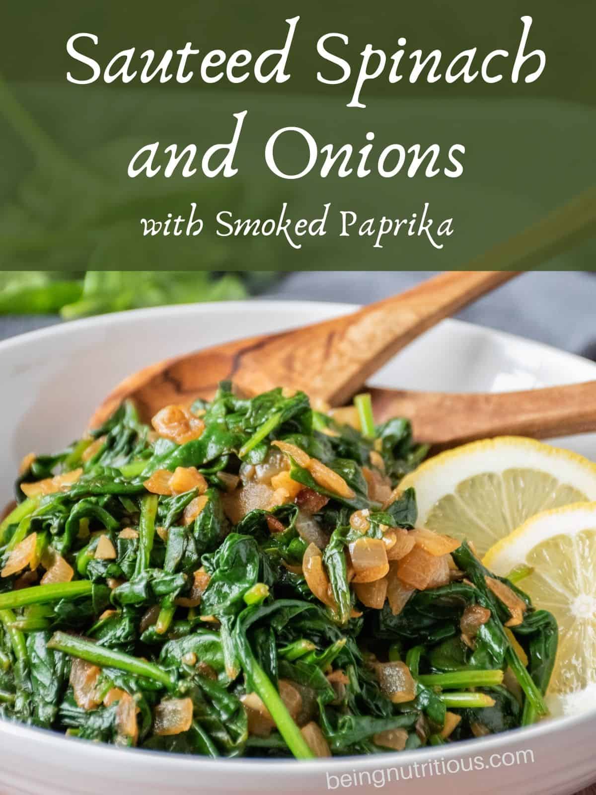 Serving bowl with sauteed spinach in it, with wooden serving spoons and garnished with lemon slices. Text overlay: Sauteed Spinach and onions with smoked paprika.
