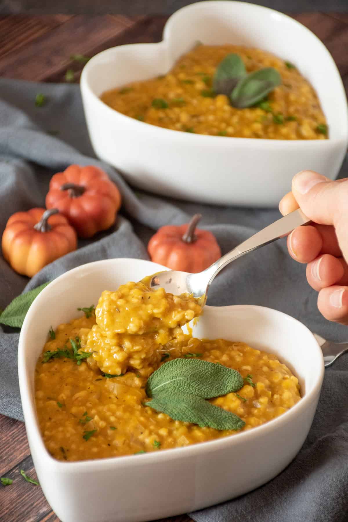 Pumpkin steel cut oats risotto in a heart shaped bowl, with a spoonful being held up.