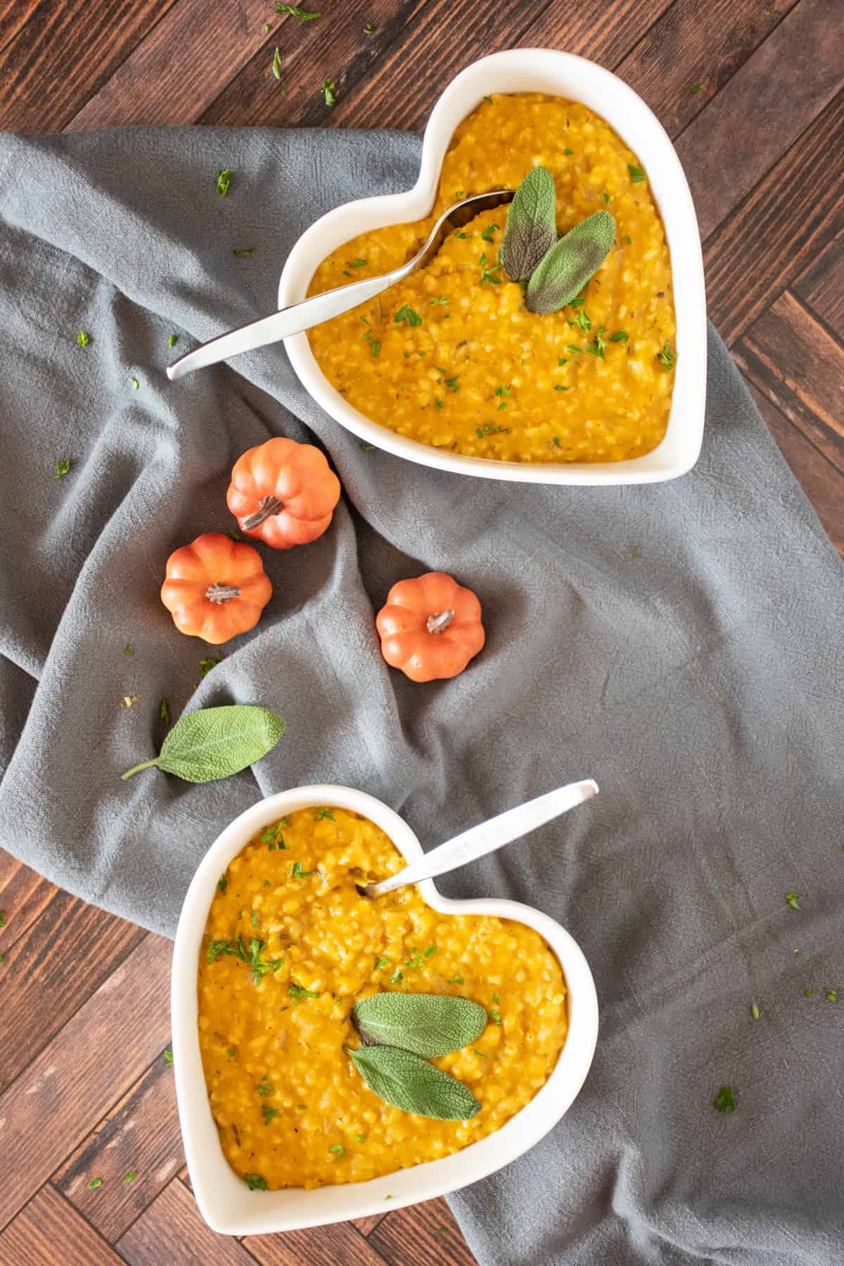 Overhead image of 2 heart shaped bowls of risotto, garnished with fresh sage leaves and chopped parsley.