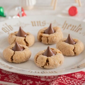 5 peanut butter cookies with chocolate kisses in them, on a serving plate.