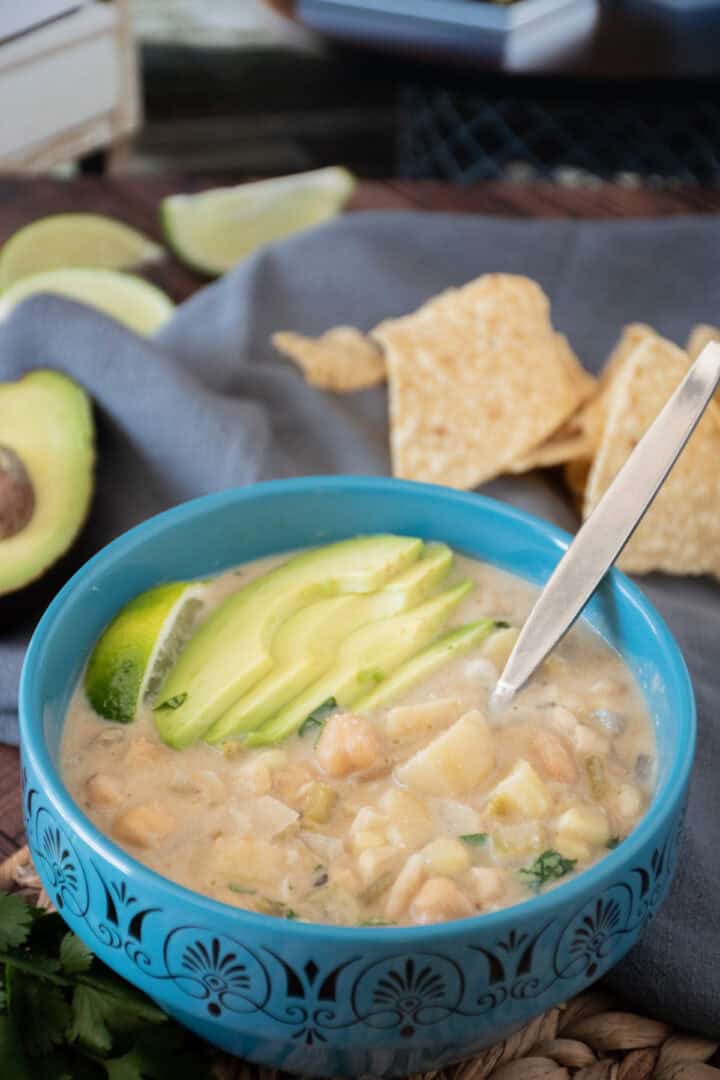Bowl of white chili, garnished with sliced avocado, a lime wedge, and chopped cilantro.