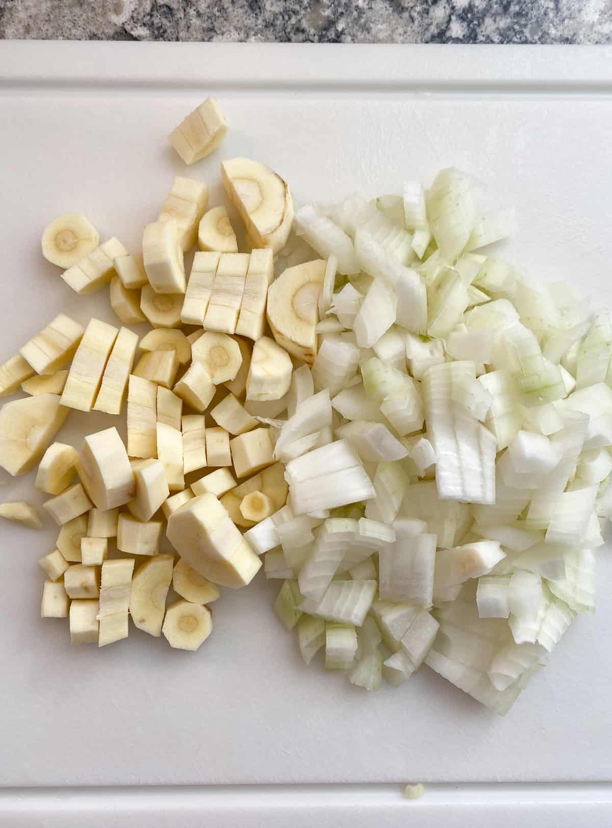 Chopped onions and parsnips on a cutting board.