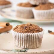 Single muffin on a dish. A stack of muffins is visible in the background.
