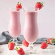 Two tall glasses of a smoothie, garnished with a fresh strawberry.