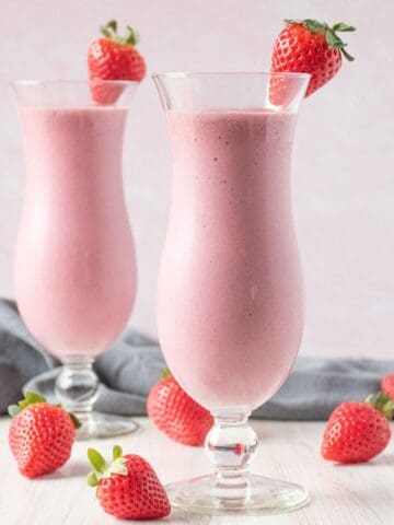 Two tall glasses of a smoothie, garnished with a fresh strawberry.