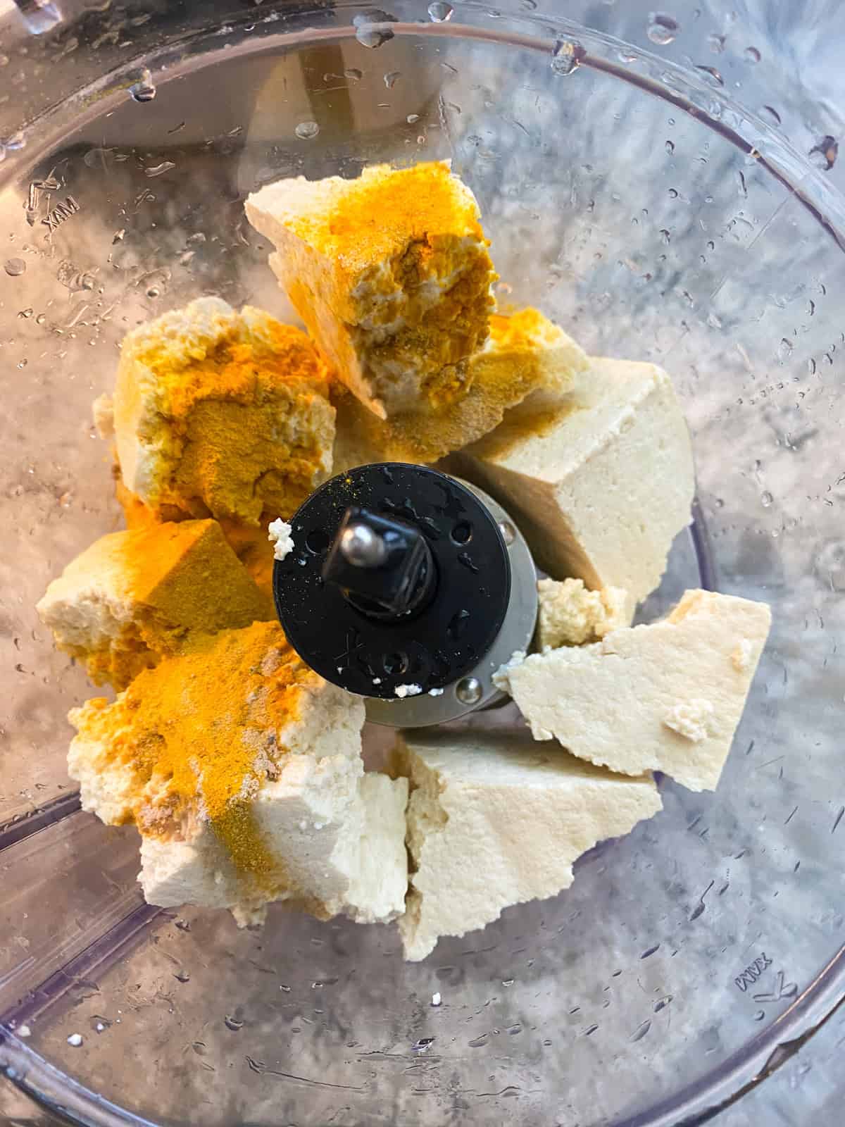 Chunks of tofu and spices in food processor.