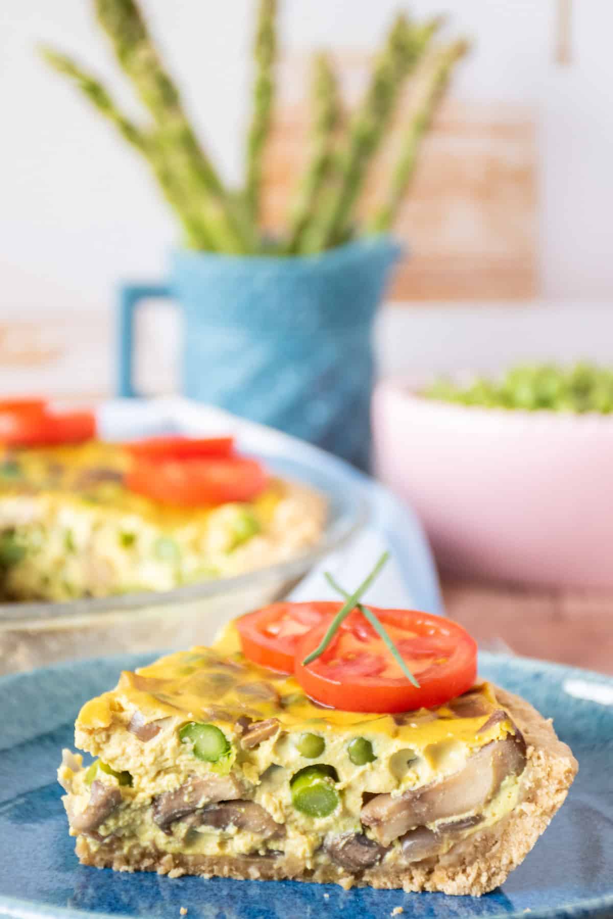 One slice of quiche on a plate, garnished with tomato slices and chives.