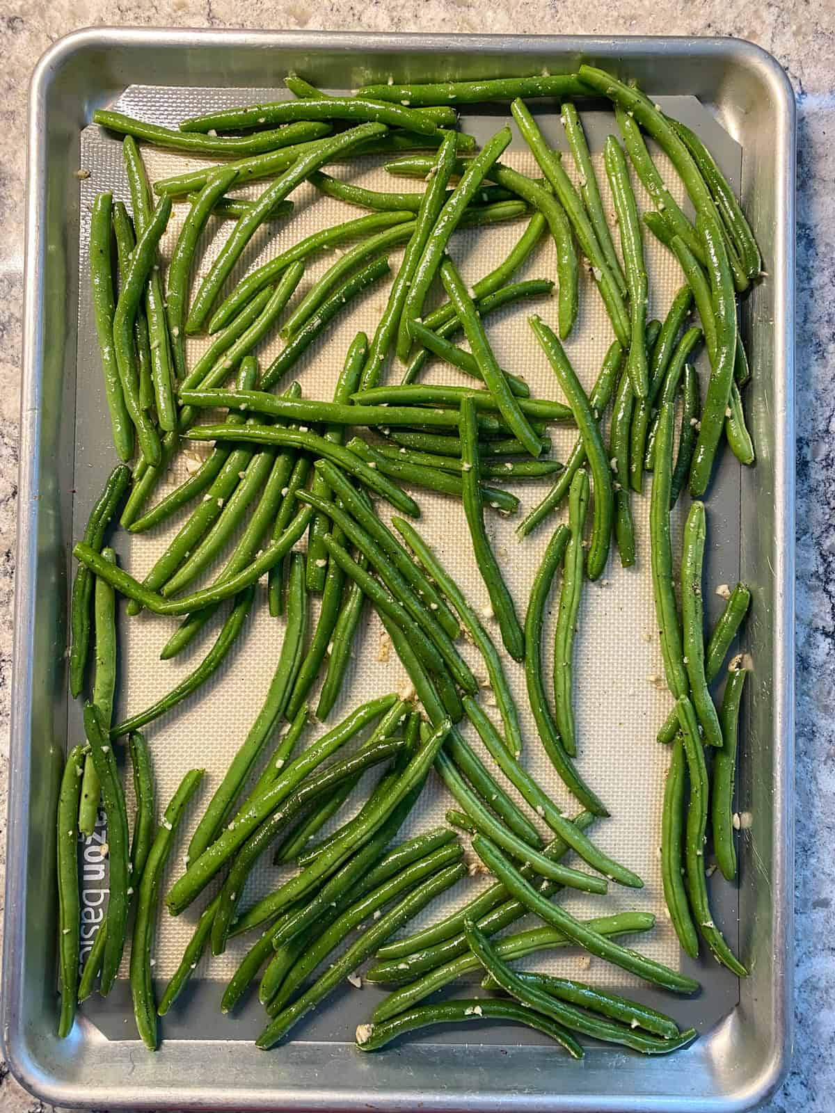 Fresh green beans, tossed with oil, garlic, salt and pepper, on a baking sheet.