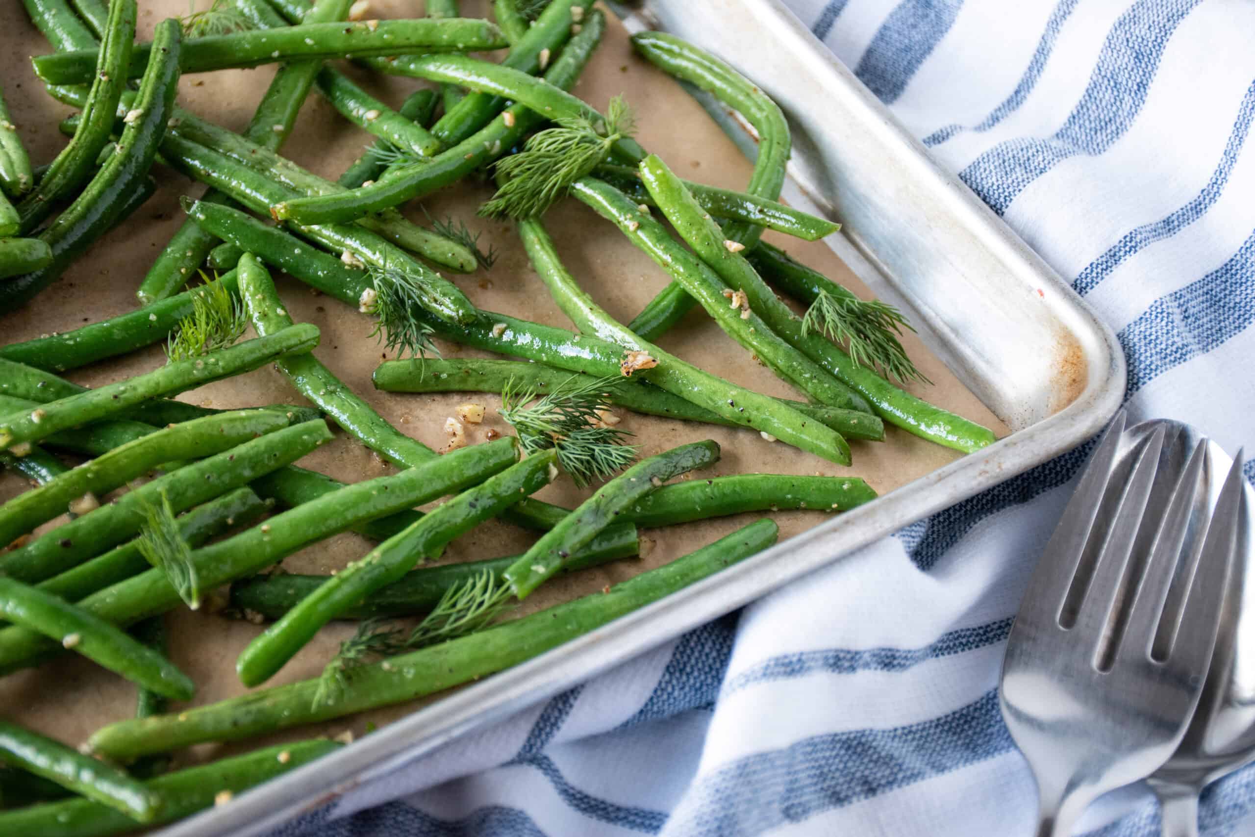 Roasted green beans on a baking sheet, garnished with fresh dill.
