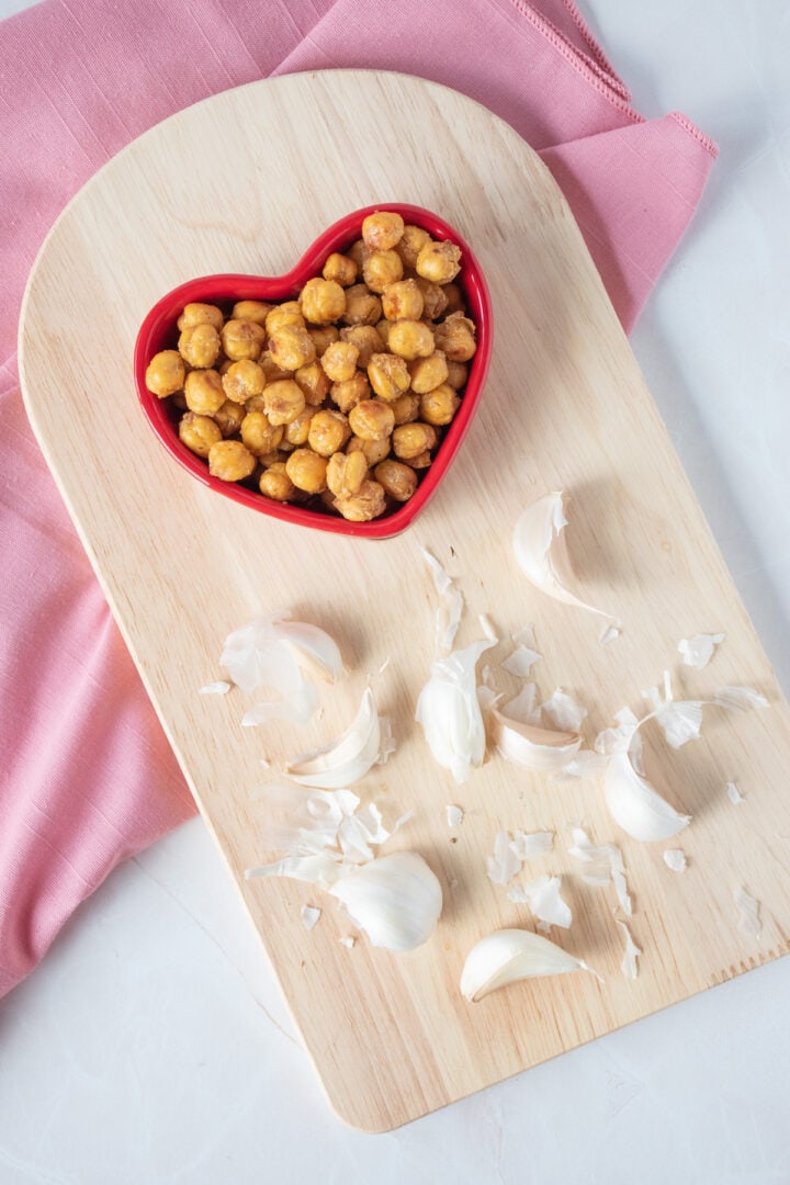 Crispy chickpeas in a heart shaped bowl, with raw garlic cloves around.